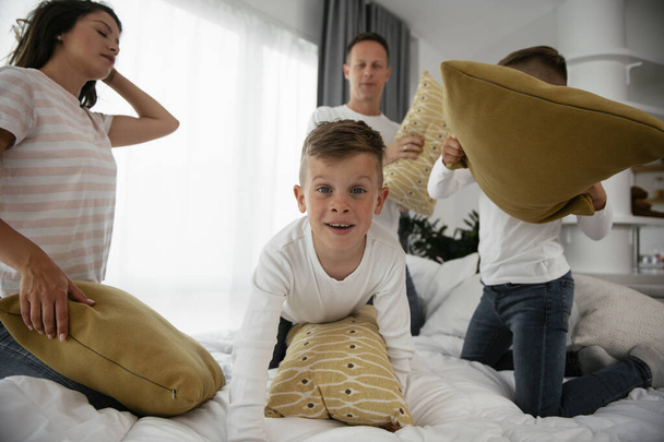 Jeunes parents avec des fils combattant des oreillers sur le lit. Heureux père et mère avec des garçons s'amuser à la maison. - Photo, image