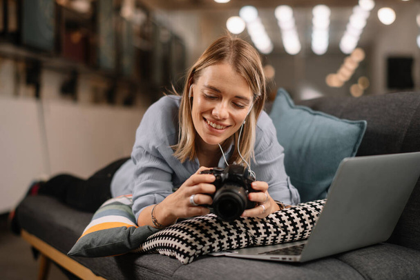 Jeune photographe féminine travaillant sur un ordinateur portable et vérifiant les photos sur l'appareil photo. - Photo, image