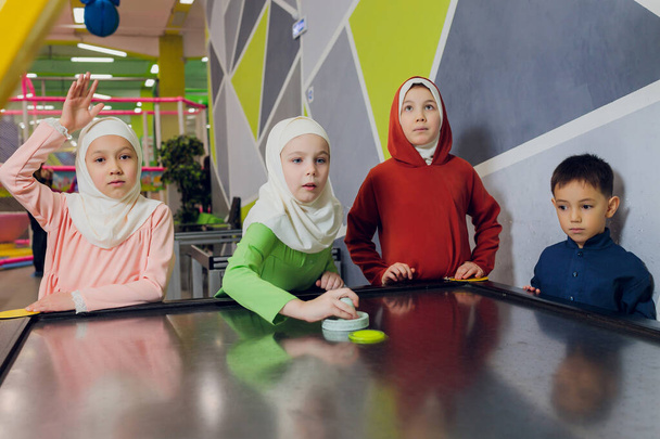 children in muslim clothes play air hockey. - Foto, afbeelding