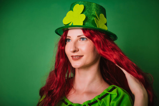 Punatukkainen pitkätukkainen tyttö vihreällä taustalla hattu shamrocks. Juhlii Pyhän Patrickin päivää. valokuva studiossa - Valokuva, kuva