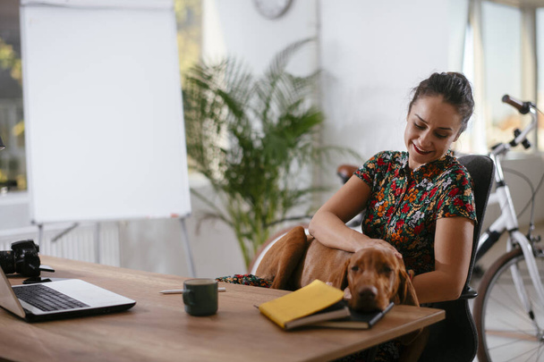 νεαρή γυναίκα επιχειρηματίας παίζει με το σκυλί της στο γραφείο - Φωτογραφία, εικόνα