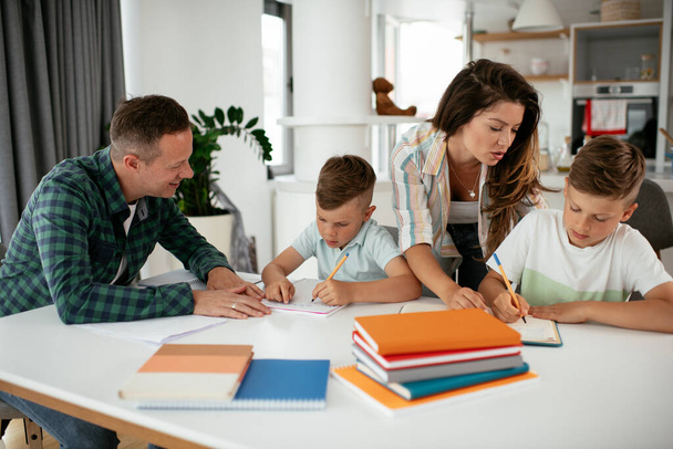 Οι γονείς βοηθούν τα παιδιά με τις εργασίες τους. Μικρά αγόρια μαθαίνουν στο σπίτι. - Φωτογραφία, εικόνα