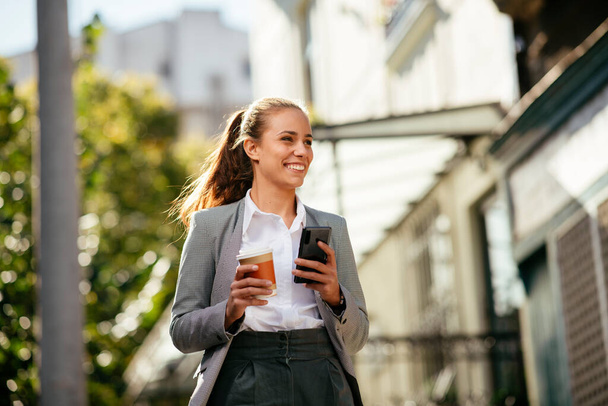 Šťastná mladá podnikatelka pomocí telefonu na ulici při kávové brzdě - Fotografie, Obrázek