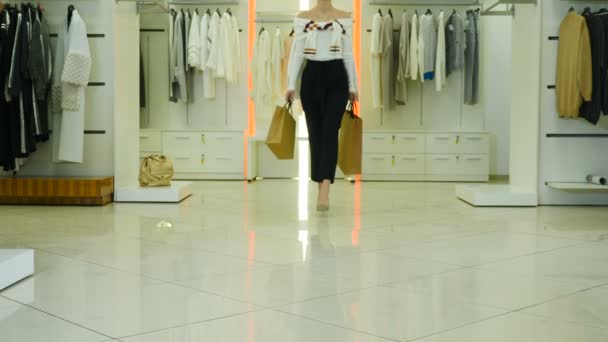 Rückansicht einer Modeeinkäuferin in einem Kaufhaus mit farbigen Taschen. Niedrige Aufnahme weiblicher Beine, die in bunten Kleidern mit Einkäufen in Taschen durch helle Modeboutiquen laufen. 4 k Video - Filmmaterial, Video
