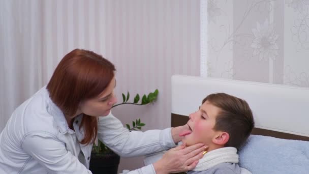 μητέρα εξετάζει ανθυγιεινή κατάσταση του αρσενικού παιδιού, μετρά τη θερμοκρασία με το θερμόμετρο μη επαφής του γιου που βρίσκεται στο κρεβάτι - Πλάνα, βίντεο