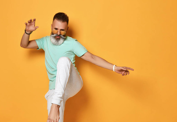 Stylish trendy gray-haired hipster guy dancing and having fun on bright orange background. - Photo, Image