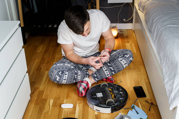 Kış süsleri ve Noel komik çoraplarıyla genç bir baba yeni yıl ve Noel tatillerinde evi temizlemek için bir robot elektrikli süpürge servis eder. Haneler için yeni teknoloji. - Fotoğraf, Görsel