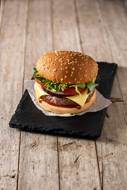 Cheeseburger with beef,tomato, lettuce and onion on wooden table - Foto, Bild