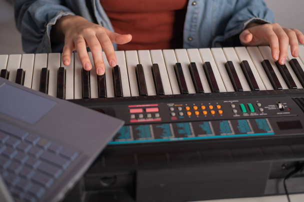 Close-up of female hands on the electric piano. A woman is learning to play the synthesizer on a laptop - 写真・画像