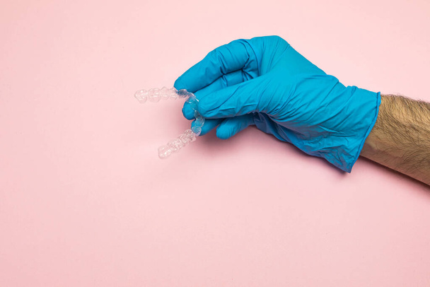 Ręka lekarza dentysty w niebieskich rękawiczkach lateksowych posiada wyraźny stabilizator zębów na różowym tle. Koncepcja aparatu dentystycznego - Zdjęcie, obraz