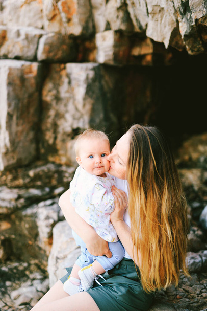 Karadağ 'da kayalık bir sahilde otururken anne bebeğini yanağından öpüyor. - Fotoğraf, Görsel