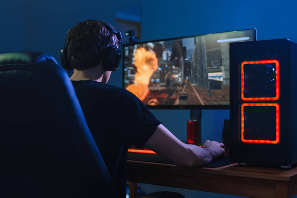 Νέοι επαγγελματίες gamer παίζουν τουρνουά online βιντεοπαιχνίδια στον υπολογιστή με ακουστικά στο δωμάτιό του, κόκκινο και μπλε νέον χρώμα. Η ιδέα του Cybersport. Πίσω όψη - Φωτογραφία, εικόνα