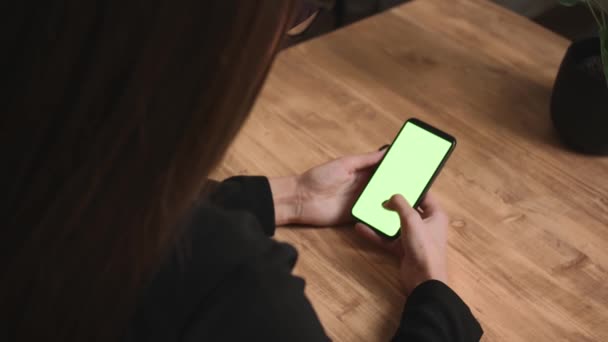 Een close-up. Achteraanzicht van vrouw met smartphone chromakey groen scherm kijken inhoud, vegen scrollen thuis of op kantoor. Begrip "gadgets". - Video