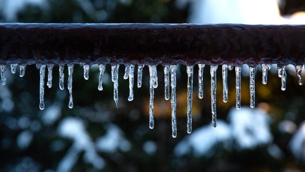 Viele kleine Eiszapfen im Winter. Eiszapfen hängen an einem braunen Rohr. Gefrorenes Wasser und Metalloberfläche, Winterzeitkonzept - Foto, Bild