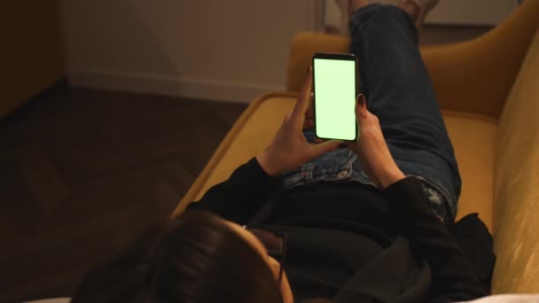 Вид сзади. Женщина, использующая телефон зеленый макет экрана хромаки лежал на диване в домашнем офисе. Девушка с помощью смартфона, просмотра Интернета, просмотра контента. Женщина разговаривает по телефону с видеозвонком. - Кадры, видео