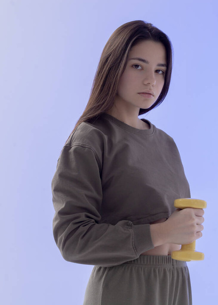 beautiful girl in colored sportswear holds a dumbbell in a bright room - Valokuva, kuva