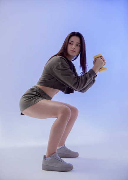 beautiful girl in colored sportswear holds a dumbbell in a bright room - Fotografie, Obrázek