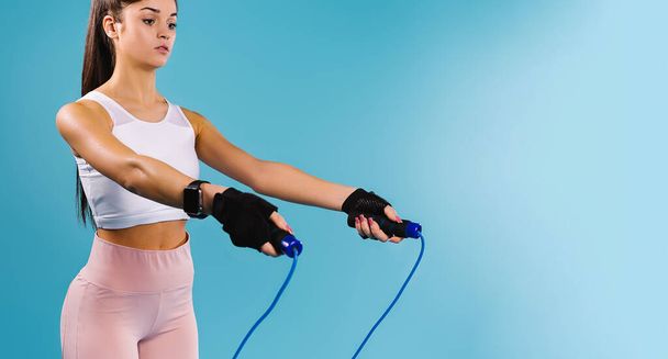 Banner,long format. Fitness and lifestyle concept. A slender girl with a skipping rope on a blue background with an empty side space where your advertisement can be. - Фото, изображение