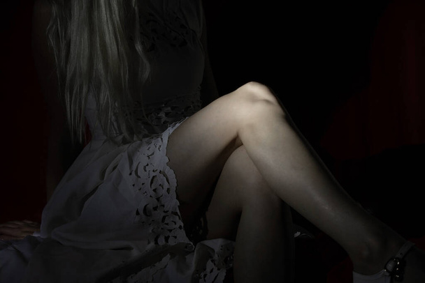jambes féminines dans une robe blanche assise dans l'obscurité, solitude - Photo, image