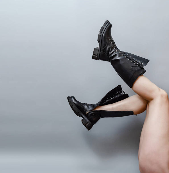 Patas femeninas levantadas en botas negras sobre fondo gris. - Foto, imagen