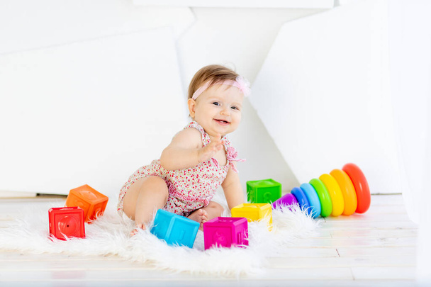 glückliches kleines Mädchen sitzt in einem weißen Raum in einem roten Kleid mit leuchtenden Spielzeugen - Foto, Bild