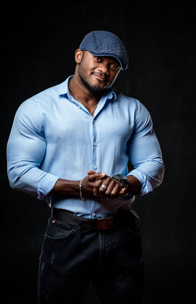 Studio portrait of black man wearing light shirt and cap posing over black artistic background. Closeup. - 写真・画像