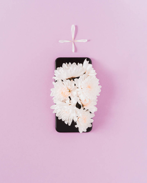 Flores de margarita blanca en un teléfono negro creando la forma de una tumba. Arte mínimo conceptual. - Foto, imagen