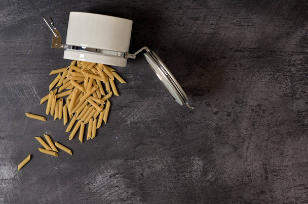 detail of a white ceramic jar with lid with macaroni inside on a dark background - Foto, afbeelding