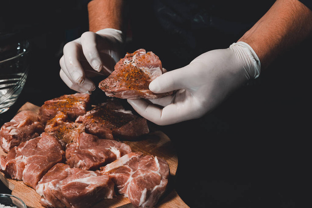 Marineren van varkensnek spiesjes, toevoegen van zout, curry en basilicum aan het vlees, stukken vlees op een houten bord.2020 - Foto, afbeelding