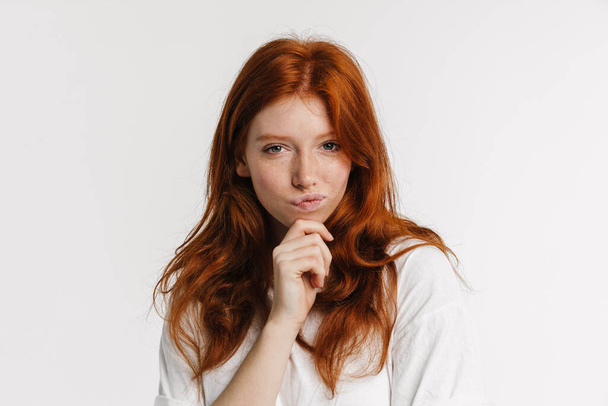 Ginger beautiful serious girl thinking and looking at camera isolated over white background - Foto, afbeelding