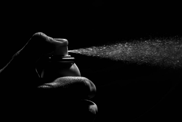 Botella pequeña de spray antibacteriano presionada por una mano desgastada con una iluminación dramática en blanco y negro. Aerosol desinfectante limpio - Foto, Imagen