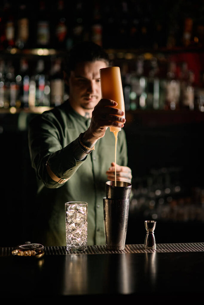 man bartender holds bottle of topping and adds it to glass of shaker - Photo, image