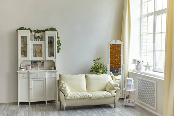 Konforlu oturma odasının içi ahşap büfe ve yastıklı beyaz kanepe, yer aynası ve büyük ışıklı pencere. - Fotoğraf, Görsel