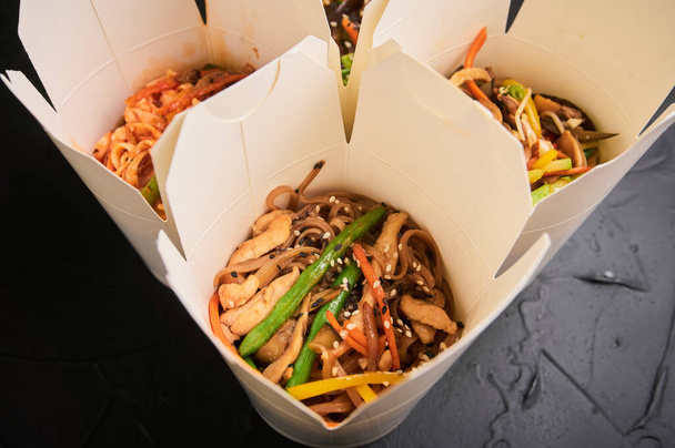 neljä laatikkoa kiinalaista ruokaa ja syömäpuikot tummalla pohjalla. - Valokuva, kuva
