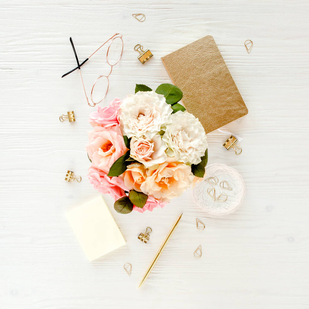 Flat lay womens office desk. Female workspace with pink roses flowers bouquet, accessories, golden diary, glasses on white wooden background Top view - Fotografie, Obrázek