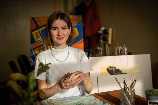 若いアーティストがアートスタジオで粘土を成形しています。アーティストのスタジオで粘土彫刻から女の子の型。陶芸店で働く実業家 - 写真・画像