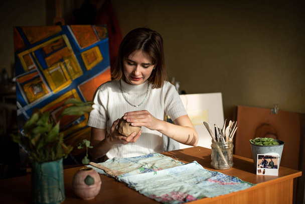 Junger Künstler formt rohe Tonerde im Kunstatelier. Mädchen formen aus Ton Skulpturen im Atelier des Künstlers. Geschäftsfrau in ihrem Töpferladen - Foto, Bild