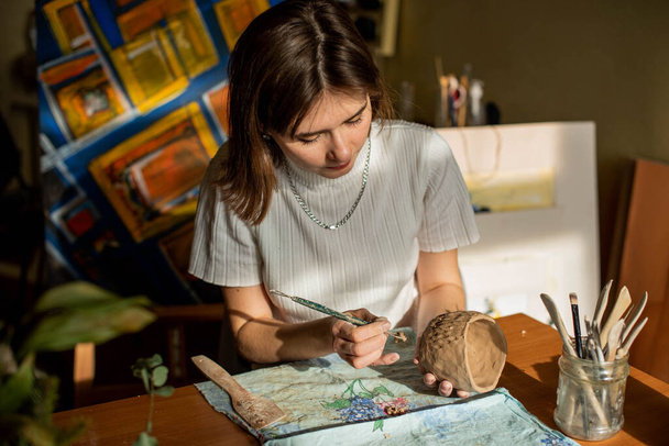mladý umělec formující syrovou hlínu v uměleckém studiu. Dívčí plísně z hliněné plastiky v ateliéru umělce. Obchodní žena ve svém obchodě s keramikou - Fotografie, Obrázek