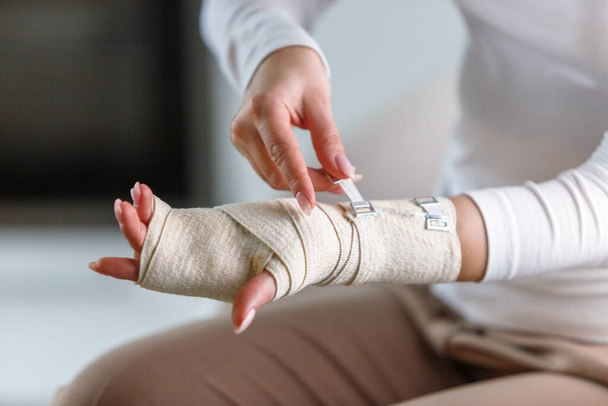 Close up da mulher envolvendo seu pulso doloroso com bandagem ortopédica elástica flexível de apoio após esportes mal sucedidos ou lesão. Síndrome do túnel do carpo, artrite, conceito de entorse de braço.  - Foto, Imagem
