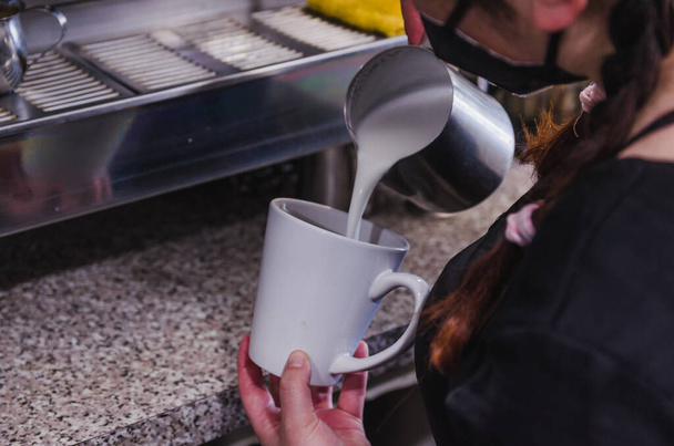 Barista Mädchen bereitet in einer Cafeteria ein Getränk auf Kaffeebasis zu, trägt schwarze Masken.  - Foto, Bild