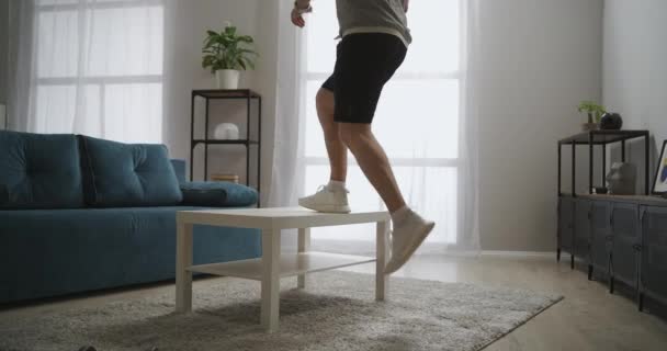 atlético homem está treinando com mesa no apartamento, fazendo exercício para pernas músculos, móveis como equipamentos esportivos em casa, estilo de vida saudável - Filmagem, Vídeo