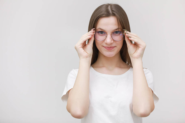 Focused frowning office girl staring at camera through eyeglasses on white background. Young woman adjusting eyewear. Glasses wearing concept. - Zdjęcie, obraz