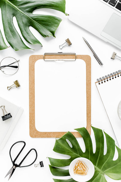 Home office workspace mockup with laptop, tropical leaves Monstera, clipboard, notebook and accessories on white background. Flat lay, top view - Foto, imagen