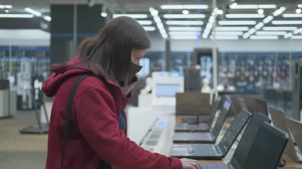 Maskiertes Mädchen telefoniert und kauft Laptop im Laden - Filmmaterial, Video
