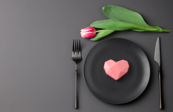 Romantic festive black festive table setting with heart and tulip on a dark background. Valentine's Day, Wedding Day, Birthday, Women's Day and Mother's Day. Flat lay. Copy space - 写真・画像