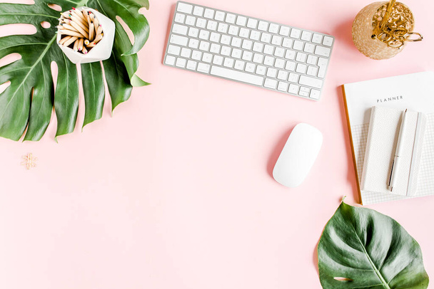 Flat lay home office desk. Female workspace with computer, tropical palm leaves Monstera, accessories on pink background. Top view background.  - 写真・画像