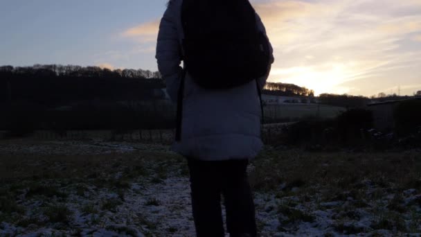 Yürüyüşçü kış manzarasında gün batımında yürüyor - Video, Çekim