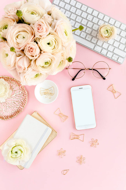 Stylized, pink womens home office desk. Workspace with computer, bouquet ranunculus and roses, phone on pink background. Flat lay. Top view. - 写真・画像