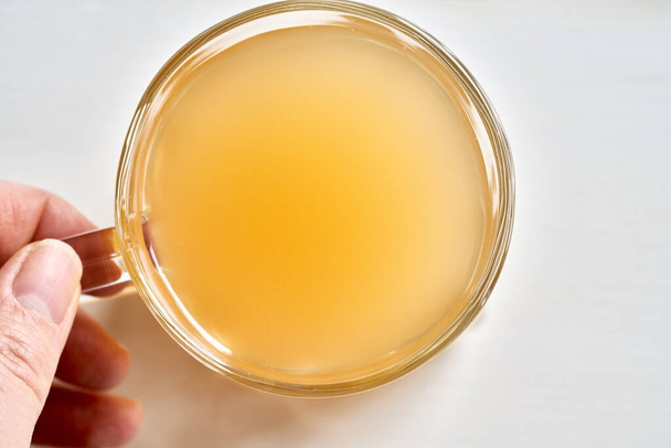 A cup of beef bone broth held by a hand on a white background, top view - Photo, Image