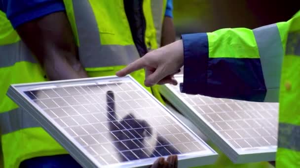 Fabrika işçisi teknisyenleri güneş pili panelini çalışan kask ve giysi ile sürdürülebilir teknoloji için gösterip kontrol ediyorlar. Konsept inşa fotovoltaik paneli yenilenebilir enerji yükle. - Video, Çekim
